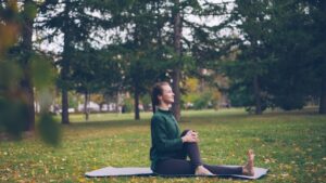 A person sits quietly on a sunny park bench surrounded by trees and greenery, reading and enjoying fresh air.