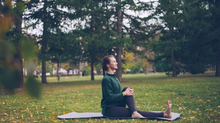 A person sits quietly on a sunny park bench surrounded by trees and greenery, reading and enjoying fresh air.