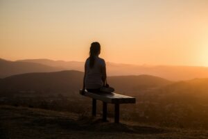 Person seated near a window practicing mindful breathing with hands resting on their lap.