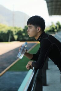 Person checking a water bottle beside hiking gear on a sunny trail